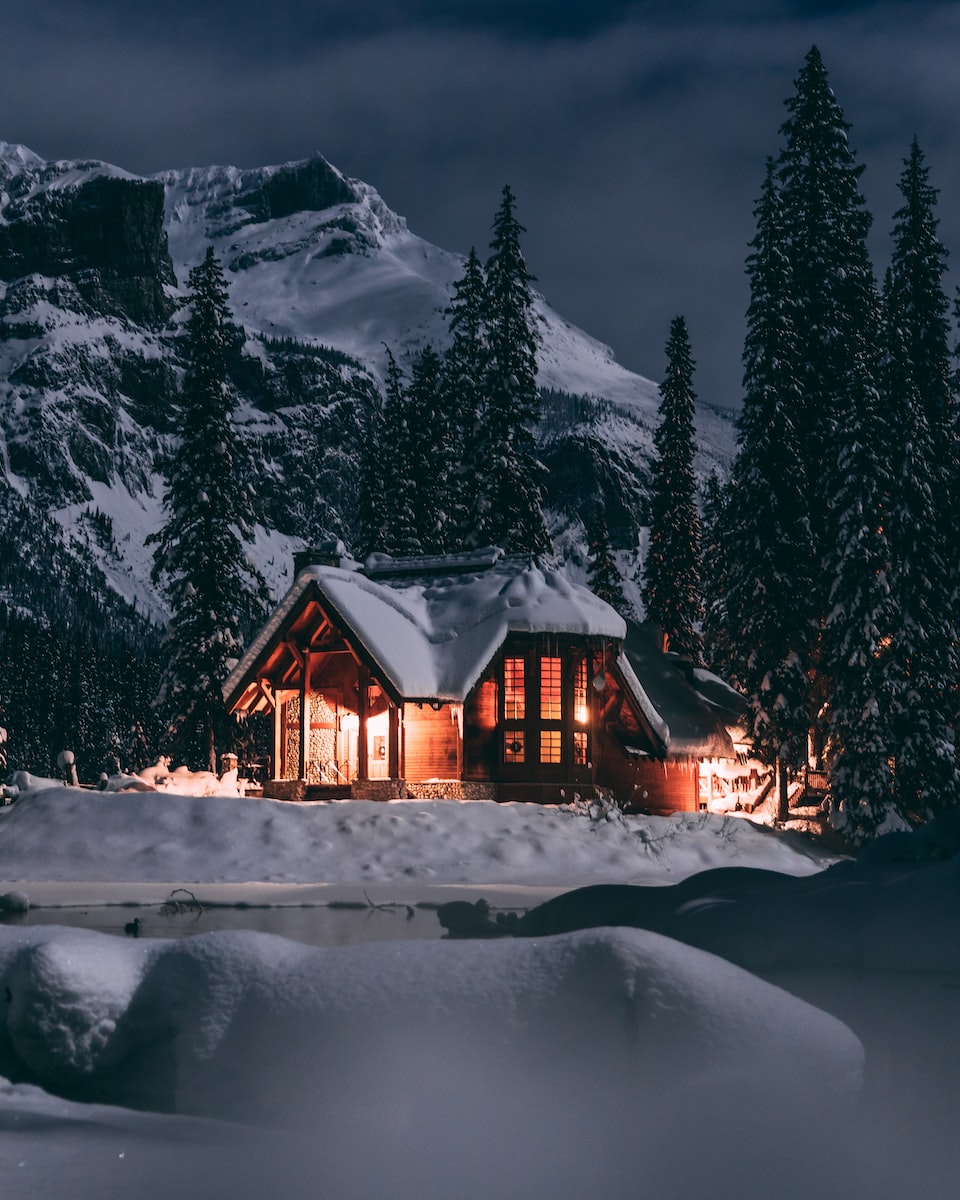 Warm erleuchtete Holzhütte bei Nacht in verschneiter Berglandschaft